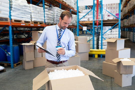 In warehouse, manager checking inventory with clipboard among stacked boxes, copy space