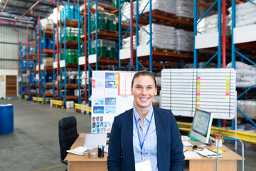 Smiling businesswoman standing in warehouse office, surrounded by inventory shelves