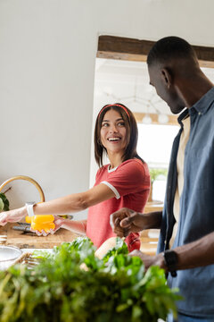 Diverse couple preparing fresh salad together in kitchen, smiling and enjoying vacation