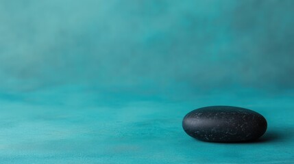 A smooth black stone rests on a textured turquoise background, creating a serene and minimalist aesthetic.
