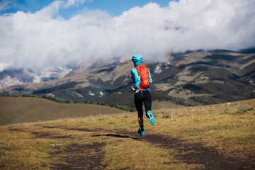 Woman trail runner running at high altitude grassland mountain top road