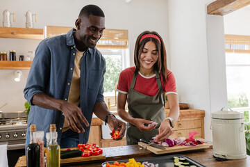 Diverse couple cooking together in kitchen, preparing fresh vegetables and enjoying time