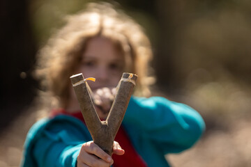 Portrait of a child shooter aiming. Funny childhood. Kids game with a slingshot. Kids handmade...