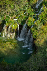 Naklejka premium Beauty in spring nature, amazing waterfall in forest. Waterfall and pond. Panoramic beautiful deep forest waterfall. Beautiful view to waterfalls with green forest. The tranquil waters of waterfalls.