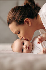 Closeup portrait of a loving mother's kiss. Happy Mother kissing her newborn baby.  Young mom kissing beautiful infant child at home. Mum loves her infant son. Happy family. Parenthood concept.