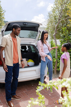 Family packing car for vacation, smiling and talking in driveway