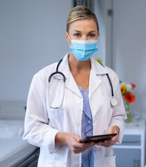 In hospital, healthcare professional using tablet, focusing on patient care with mask