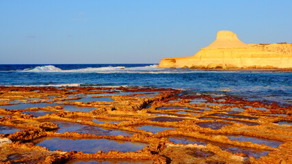 Salt pans, salterns or salt evaporation ponds in the Gozo afternoon sun with blue sea. Orange...