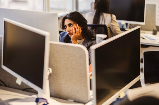 Bored businesswoman resting chin in hand at office cubicle