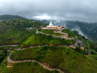 The image captures the Mahamevnawa Buddhist Monastery in Ella, Sri Lanka, perched atop a lush green...