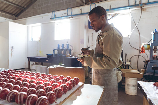 Inspecting cricket balls in factory, African American man focusing on quality control, copy space