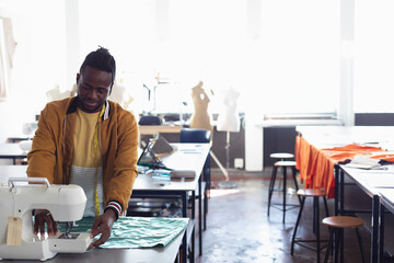Fashion student sewing fabric on machine in classroom, concentrating on design, copy space