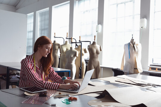 Fashion student designing clothing patterns on laptop in bright classroom studio