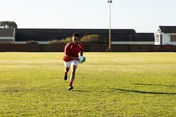 Female rugby player running with ball on field, focused and determined