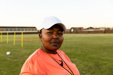 Confident female rugby coach standing on field wearing cap and whistle