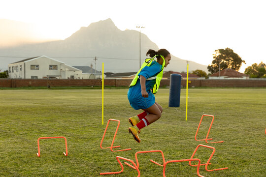 Female rugby player jumping over hurdles on field during training session