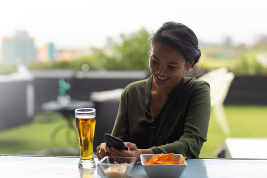 Smiling woman on rooftop enjoying snacks and checking phone during sports event - Powered by Adobe