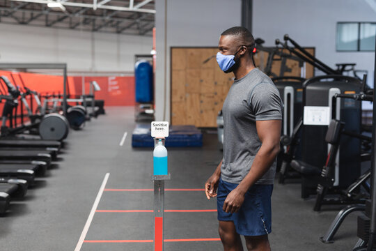 Man in gym wearing mask using hand sanitizer before workout, staying safe, copy space