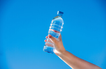 A girl holds a bottle of drinking water in her hand against a blue sky background
