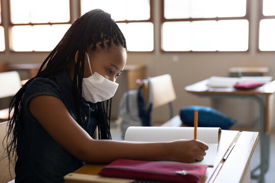 In school, young girl wearing mask writing in notebook, concentrating on task