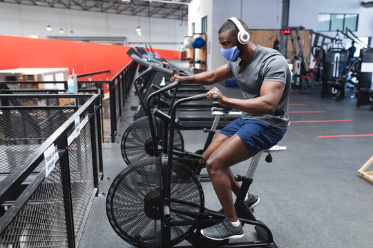 Man wearing mask and headphones cycling on exercise bike in gym