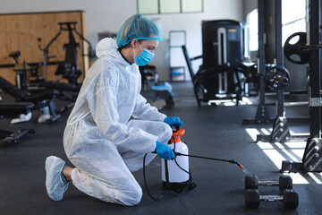 Sanitizing gym equipment, healthcare worker in protective gear ensuring safety during pandemic