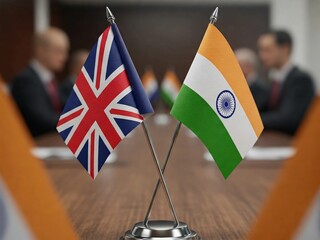 Close-up of India and UK flags on a conference table, symbolizing diplomacy, international relations, and business partnerships. Blurred background with delegates in a formal meeting setting.