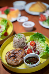 A set of pork and chicken steaks, bread and a plate of salad on a brown wooden table in a restaurant.