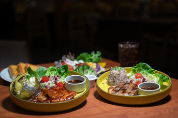 A set of pork and chicken steaks, bread and a plate of salad on a brown wooden table in a restaurant.