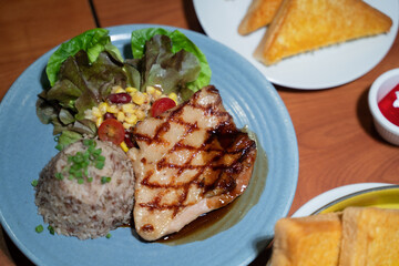 Chicken steak set with sauce, bread and salad plate on a brown wooden table in a restaurant.