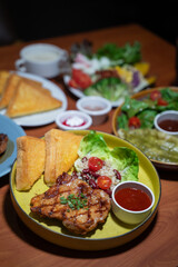 Chicken steak set with sauce, bread and salad plate on a brown wooden table in a restaurant.