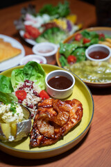Chicken steak set with sauce, bread and salad plate on a brown wooden table in a restaurant.