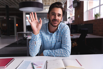 Businessman in office raising hand during video call, engaging in conversation