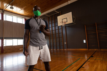 Basketball coach in gym holding whistle, wearing mask, ready for training, copy space