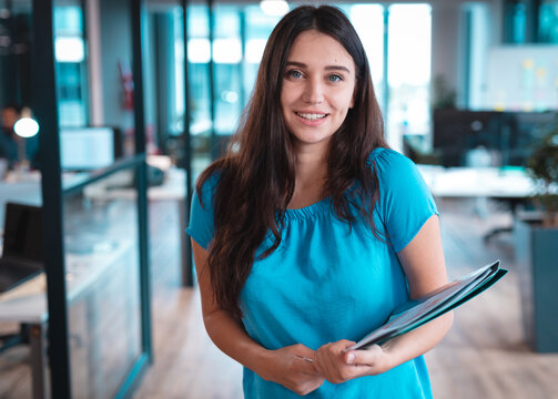 Smiling woman holding documents in modern office, ready for business meeting