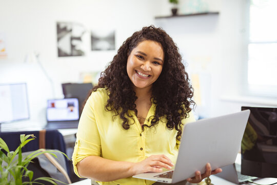 Smiling woman using laptop in modern office, feeling confident and productive