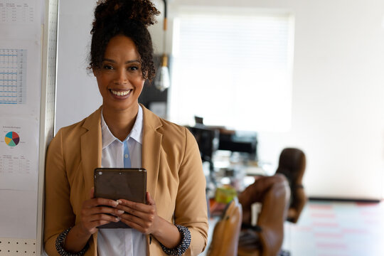 In office, businesswoman standing confidently holding tablet, smiling at camera, copy space