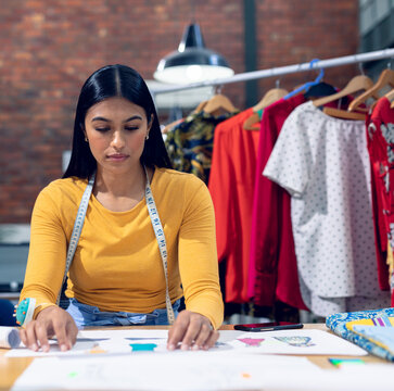 Designer sketching new clothing designs in studio, surrounded by colorful garments