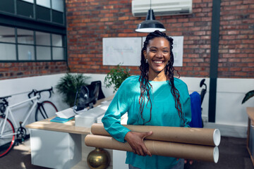 African American woman holding blueprints in modern office, smiling confidently, copy space