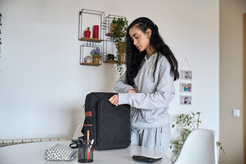 Young woman preparing backpack at home office