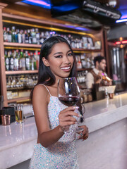 A glamorous woman in a sparkling sequin dress holding a glass of red wine at an elegant bar. She smiles confidently, radiating sophistication and charm. The luxurious bar setting