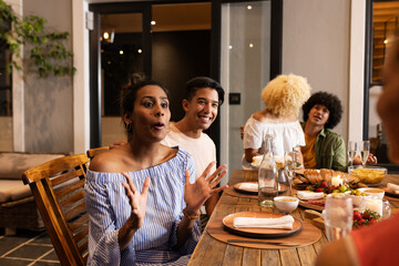 Diverse friends enjoying dinner party, laughing and sharing stories at patio table