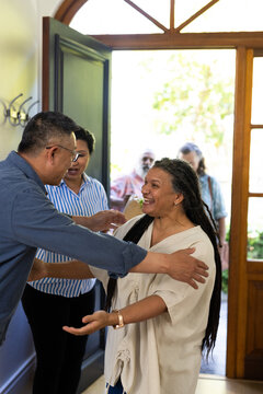 woman greeting senior diverse friends at home, smiling and welcoming them warmly