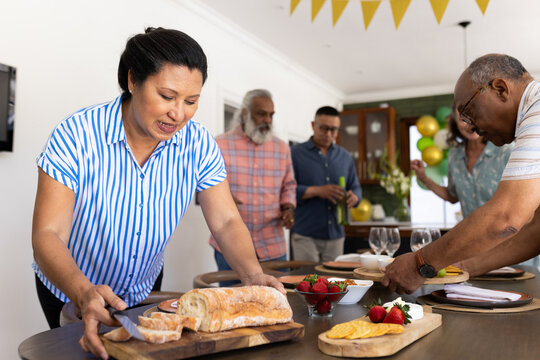 Diverse group of diverse senior friends enjoying meal preparation together at home, sharing smiles