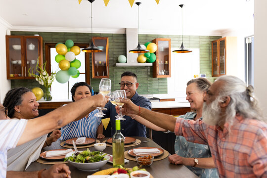 Senior diverse friends celebrating together at home, raising glasses and smiling joyfully