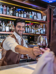 Bartender giving glass of wine to woman customer at bar counter .