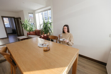 Woman drinking tea and eating a cake in her kitchen