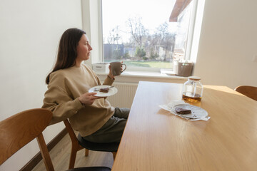 Woman drinking tea and eating a cake in her kitchen