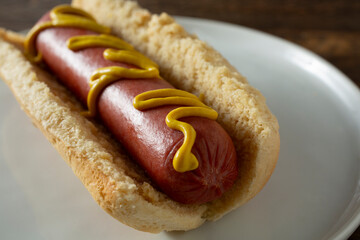 A closeup view of a hot dog topped with yellow mustard.