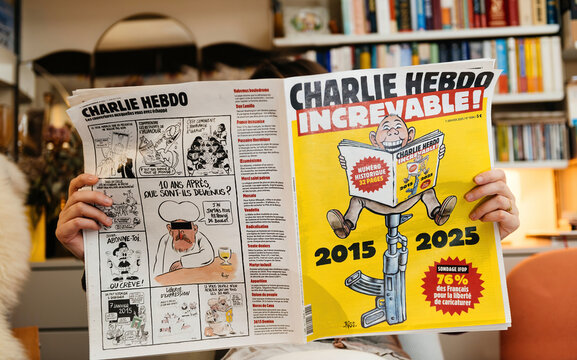 Paris, France - Jan 21, 2025: A person holding a Charlie Hebdo satirical newspaper featuring a 10-year anniversary edition, with bold cartoons and a yellow commemorative cover.